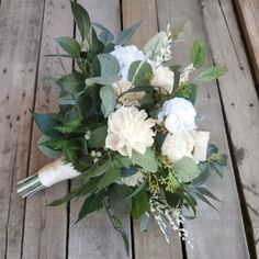 a bouquet of white flowers and greenery on a wooden floor with wood planks