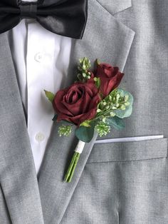 a boutonniere with red roses and greenery on the lapel of a suit