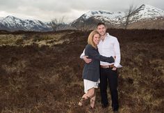 a man and woman hugging in the middle of a field with mountains in the background