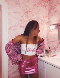 a woman standing in front of a bathroom mirror wearing a pink skirt and crop top