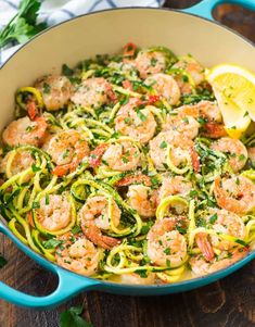 shrimp and zucchini pasta with lemon wedges in a blue skillet on a wooden table