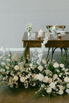 flowers and candles sit on the floor next to a table with two vases filled with white flowers