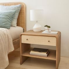 a nightstand with books on it next to a bed