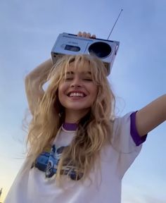 a woman with long blonde hair holding up a radio on her head and smiling at the camera