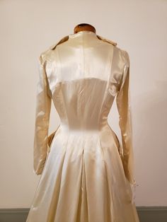 "1950s, 34\"bust,wedding ensemble consists of gown and coat of egg shell white rayon slipper satin. Gown has crystal beading at bosom, in a bow motif. Bodice of gown is strapless, with stays sewn into the interior of bodice, bodice comes to a point at waist. Skirt is full, fuller in back, and a bit longer in back than front. Coat has rounded lapels, buttons at mid section with 5 round satin buttons. Skirt of coat is floor length in front, with a cathedral length train in back. Faux pockets are a Cream Ball Gown For Evening, Cream Satin Gown With Fitted Bodice, Formal Cream Satin Gown, Cream Satin Evening Wedding Dress, Cream Ball Gown For Formal Occasions, Vintage Fitted Wedding Dress For Debutante Ball, Vintage Ball Gown Wedding Dress For Formal Occasions, Victorian Dress With Boned Bodice For Weddings, Regency Style Fitted Wedding Gown