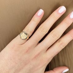 a woman's hand wearing a gold ring with a coin on the middle finger