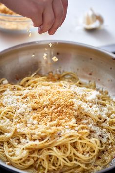 someone sprinkling parmesan cheese on top of spaghetti in a skillet