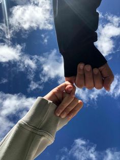 two hands holding each other in front of a blue sky with white clouds and sun