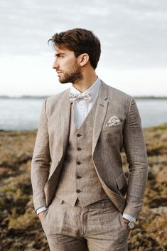 a man in a suit and bow tie standing by the water with his hands in his pockets