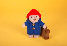 a small teddy bear wearing a red hat and blue coat holding a piece of wood