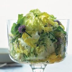 a glass bowl filled with salad on top of a white table next to a plate