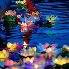 paper boats floating on top of water with people standing around them and lights in the water