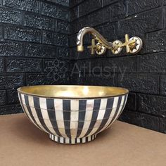 a black and white striped bowl sink with gold faucet on the wall behind it