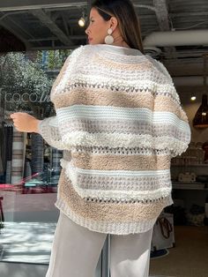 a woman standing in front of a store window wearing a sweater and pants with stripes