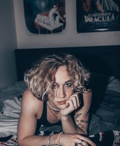 a woman laying on top of a bed next to a wall with posters above her