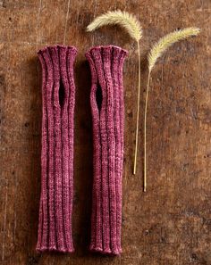 two purple knitted gloves sitting on top of a wooden table next to dry grass