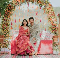 a man and woman sitting next to each other in front of a flower covered stage