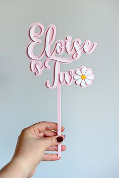 a hand holding a pink cake topper with the words please and true on it