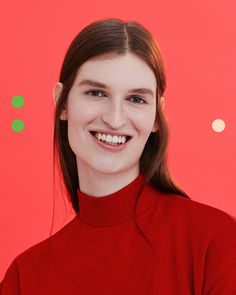 a woman in a red sweater smiles at the camera while standing against a pink and green background