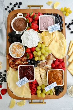 a wooden platter filled with cheese, fruit and dips