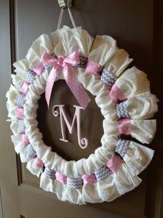 a white wreath with pink and gray bows hanging on the front door, next to a monogrammed initial