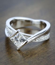 a princess cut diamond ring on top of a wooden table