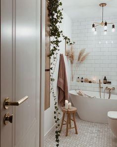 a bathroom with white tiles and plants growing on the wall next to the bathtub