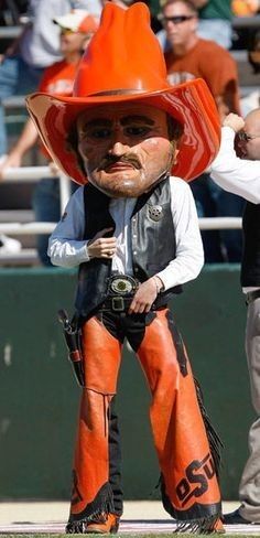 a man in an orange cowboy hat standing next to a giant fake person with his arm out