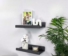 two black floating shelves with pictures and candles on them in a white living room next to a potted plant