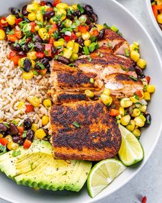 a white bowl filled with chicken, rice and veggies next to lime wedges