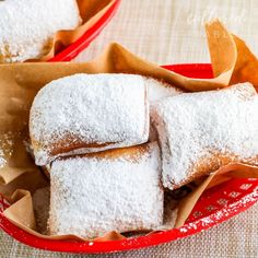 powdered sugar covered pastries sit in a red basket on a tablecloth with napkins