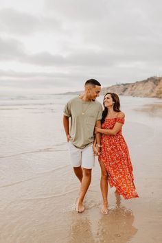 an engaged couple standing on the beach in front of the ocean during their engagement session