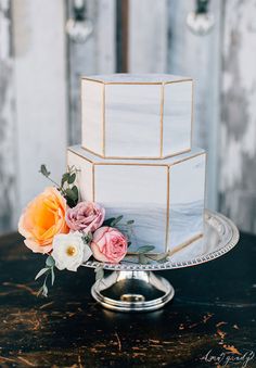 a three tiered white cake with pink and orange flowers on top sits on a table