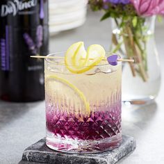 a purple and yellow drink sitting on top of a counter next to a vase filled with flowers