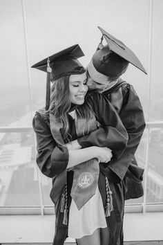 black and white photograph of two graduates hugging each other in graduation gowns on top of a building