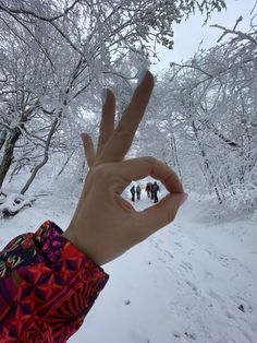 a person's hand making the peace sign in front of some snow covered trees