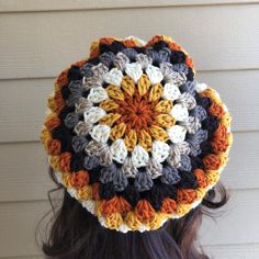 a woman wearing a crocheted hat with an orange, white and black flower