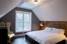 a bed sitting under a window in a bedroom next to a wooden desk and chair