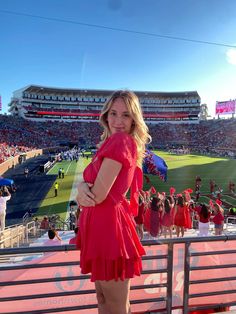 a woman in a red dress is standing on the bleachers at a football game