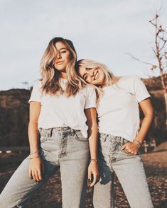 two beautiful young women standing next to each other in front of a field with trees