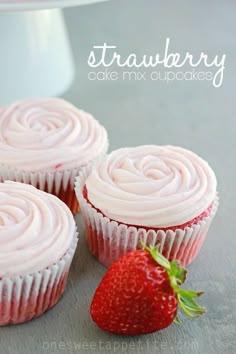 three strawberry cupcakes with frosting and a strawberry on top, sitting next to each other