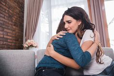 two people sitting on a couch hugging each other