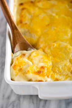 a white casserole dish filled with cheese and bread topped with a wooden spoon