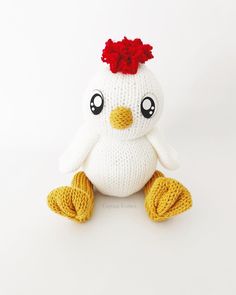 a white stuffed chicken with a red flower in its hair sitting on a white surface