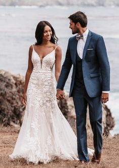 a bride and groom holding hands while standing on top of a hill next to the ocean