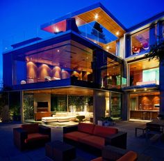 a large modern house with lots of windows and furniture in the front yard at night