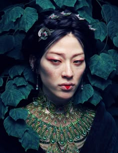 a woman with green leaves on her head and red lipstick in front of her face