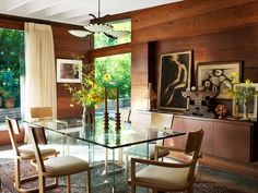 a glass dining table surrounded by chairs in a room with wood paneling and windows