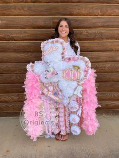 a woman in pink and white holding a large teddy bear with feathers on it's back