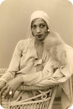 a woman sitting on a chair with a fur stole around her neck and wearing a head scarf